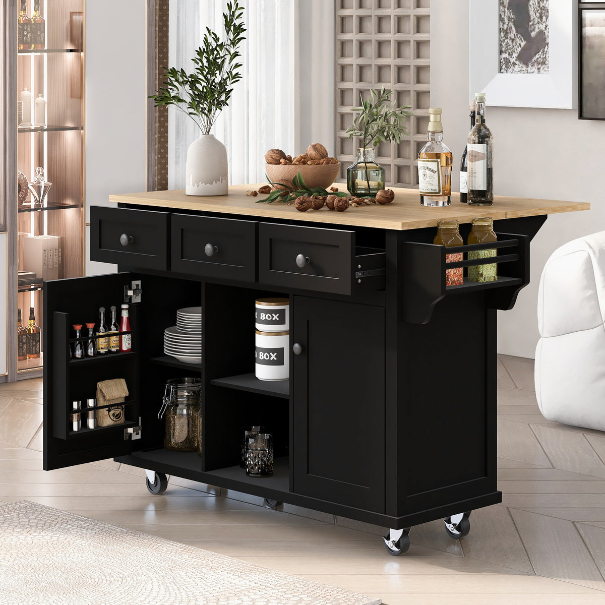 Angled view of a black kitchen island with open drawers, one open cabinet door, and a stocked side spice rack.