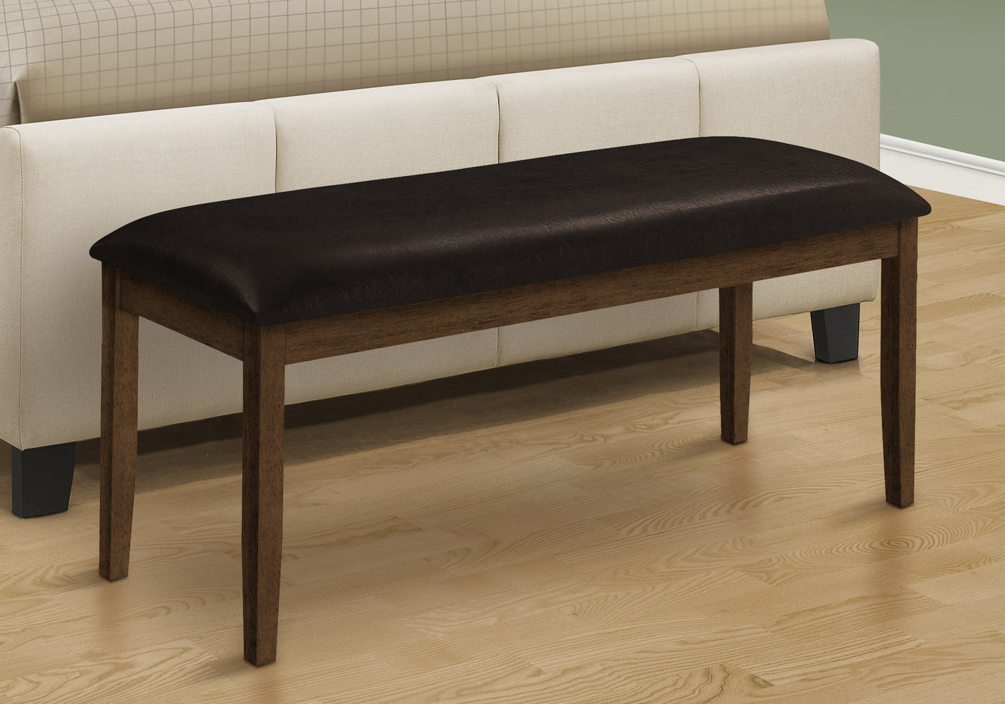 Wooden bench with black cushion in front of a beige sofa on a wooden floor.