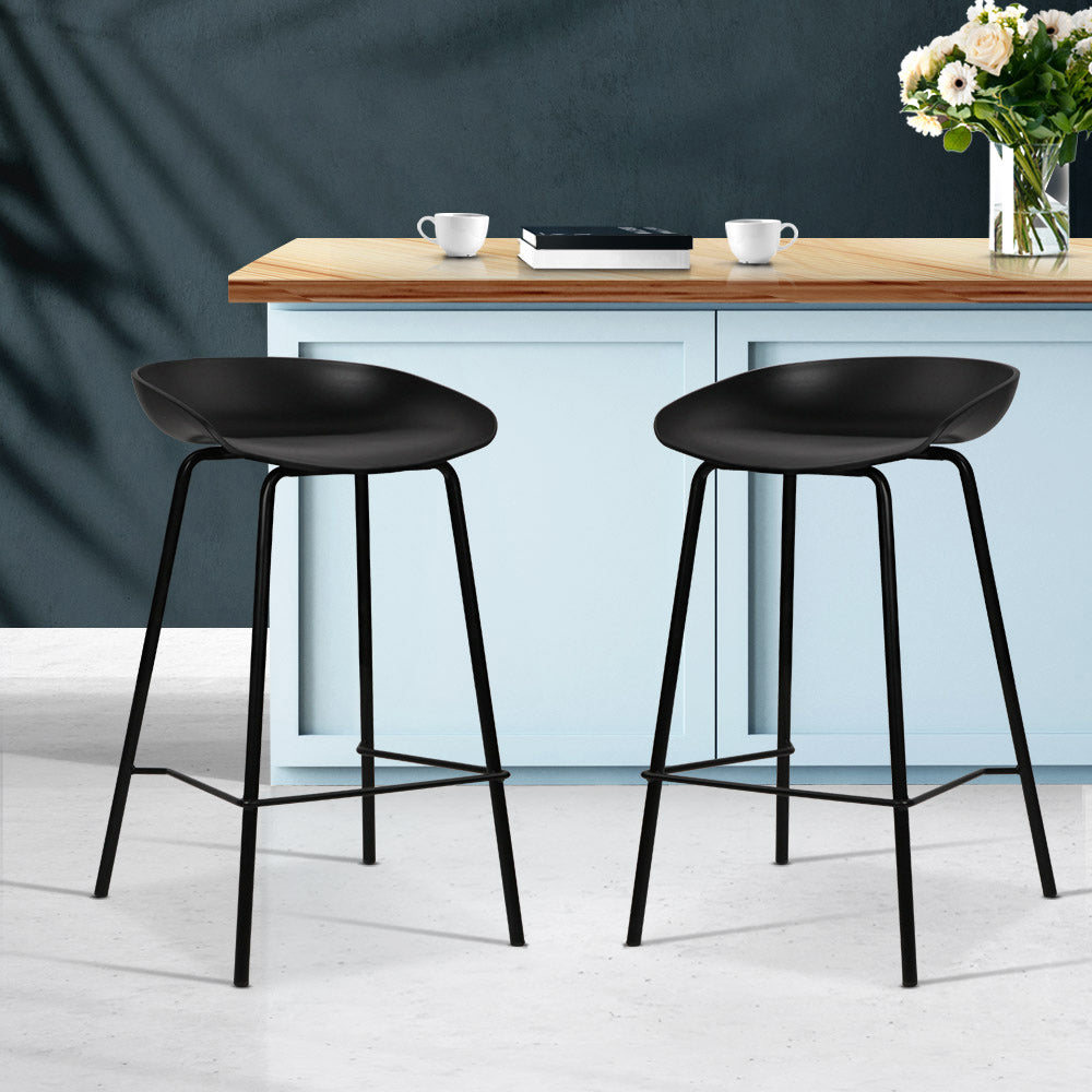 Two black bar stools in front of a kitchen counter with a dark curtain background.