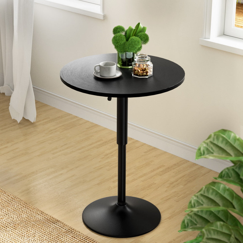 Black round table with a cup, saucer, and decorative items in a room with light wood flooring and a plant.