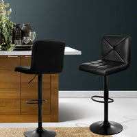 Two black bar stools in a modern kitchen setting with a dark wall and wooden cabinets.