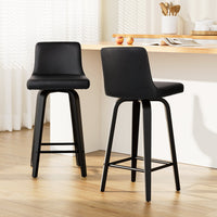 Two black bar stools in a kitchen setting with a wooden table and white walls.