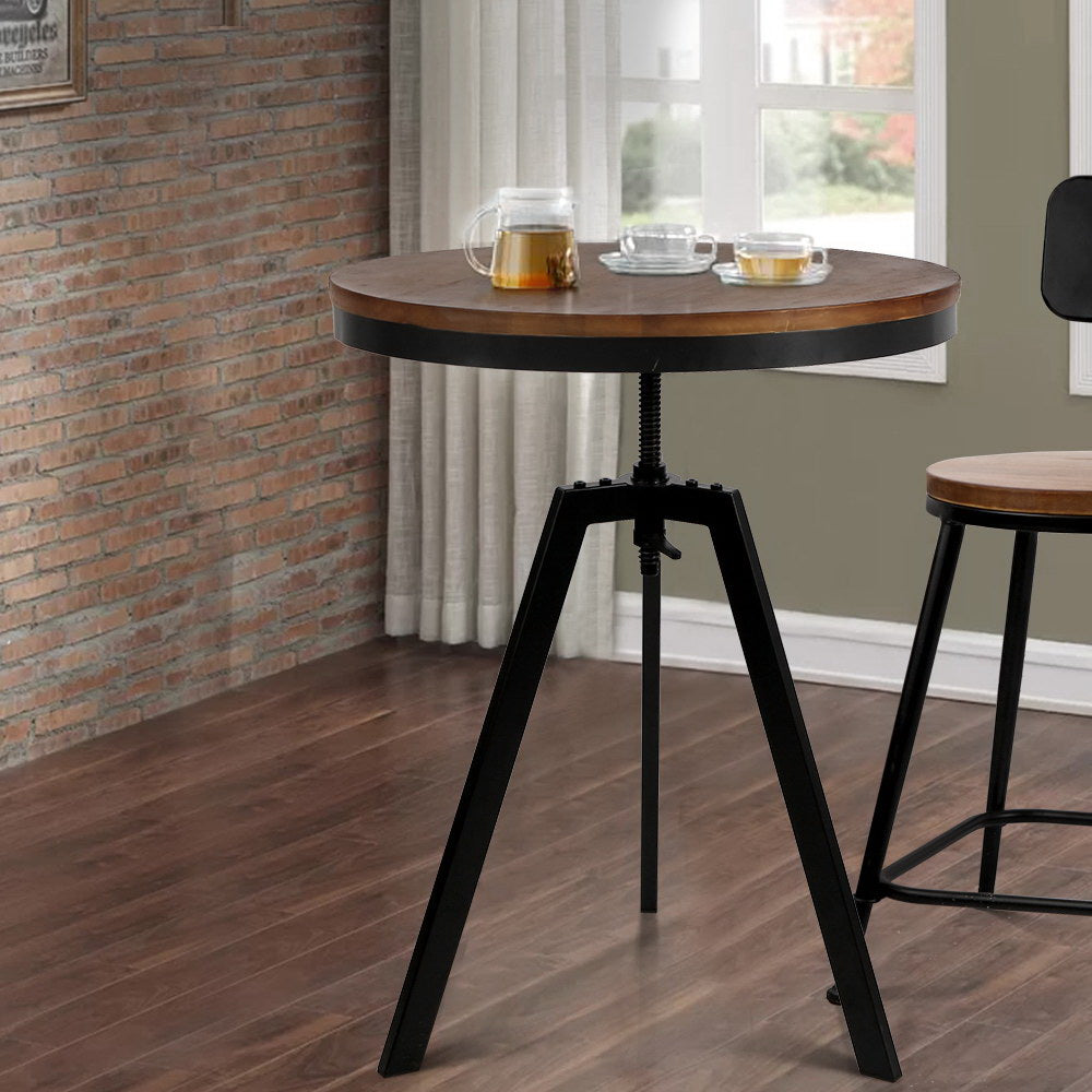 Round wooden table with black metal legs in a room with a brick wall and window.
