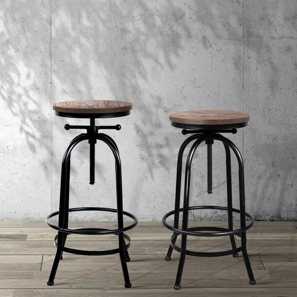 Two bar stools with wooden seats and black metal frames against a concrete wall.