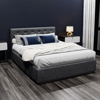 Gray upholstered bed with white bedding and blue pillows in a bedroom setting.
