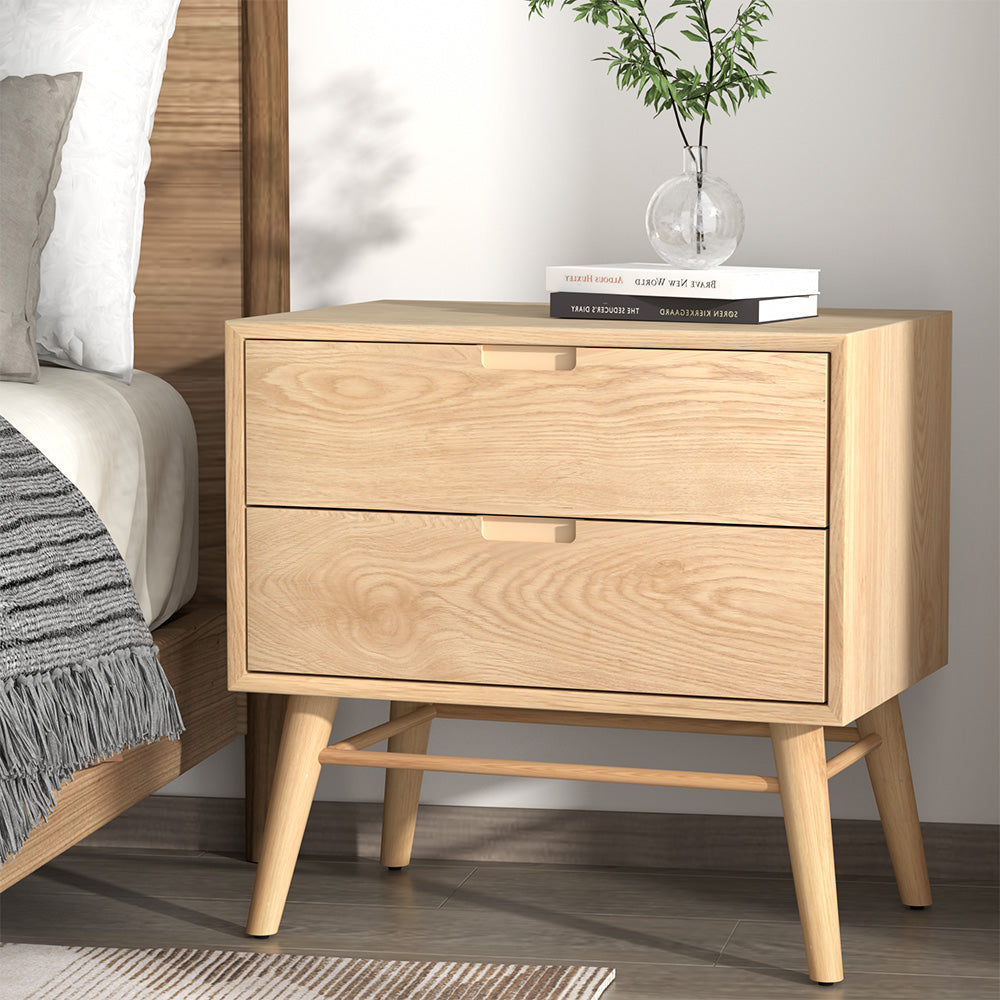 Wooden nightstand with two drawers next to a bed in a bedroom setting.