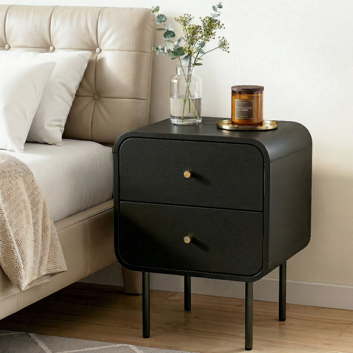 Black nightstand with two drawers next to a bed with beige headboard and white pillows.