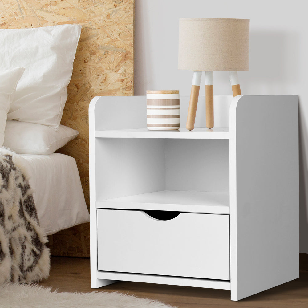 White nightstand with a drawer next to a bed with white pillows and a wooden headboard.