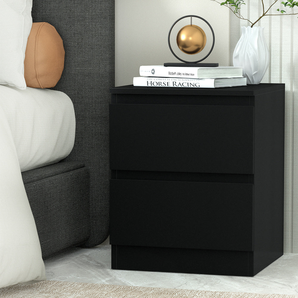 Black nightstand with books and decor items next to a bed