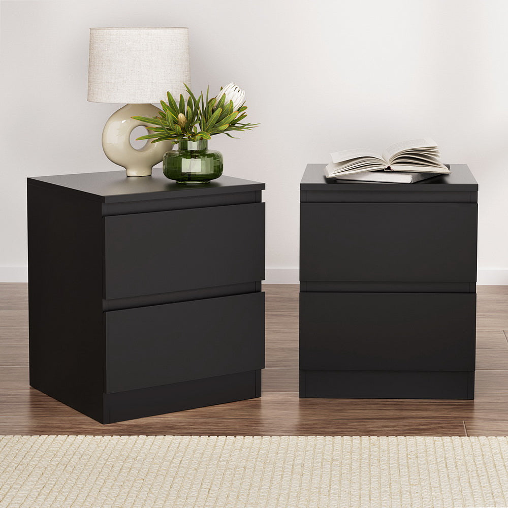 Two black nightstands with a lamp, vase, and book on a wooden floor.