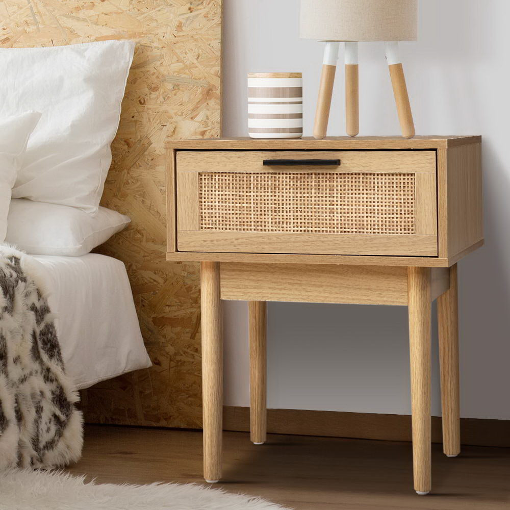 Wooden nightstand with wicker drawer next to a bed with white pillows.