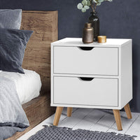 White nightstand with two drawers next to a bed with wooden headboard