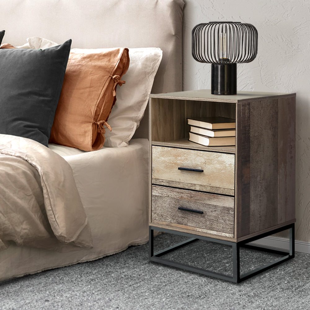 Wooden nightstand with books and a lamp next to a bed with pillows.