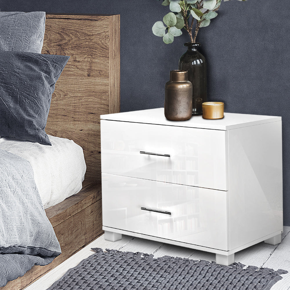 White nightstand with two drawers next to a bed with wooden headboard and gray bedding.