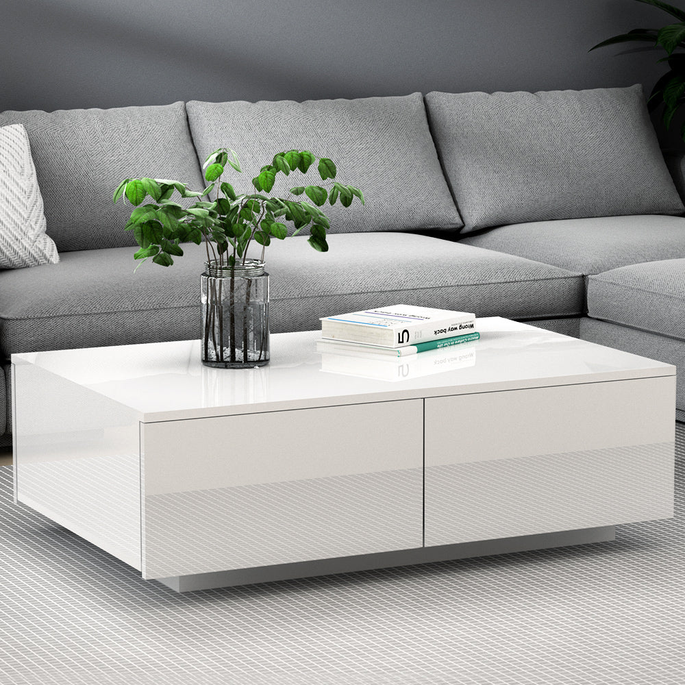 White coffee table with a vase of greenery and books in front of a gray sectional sofa.