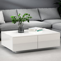 White coffee table with a vase of greenery and books in front of a gray sectional sofa.