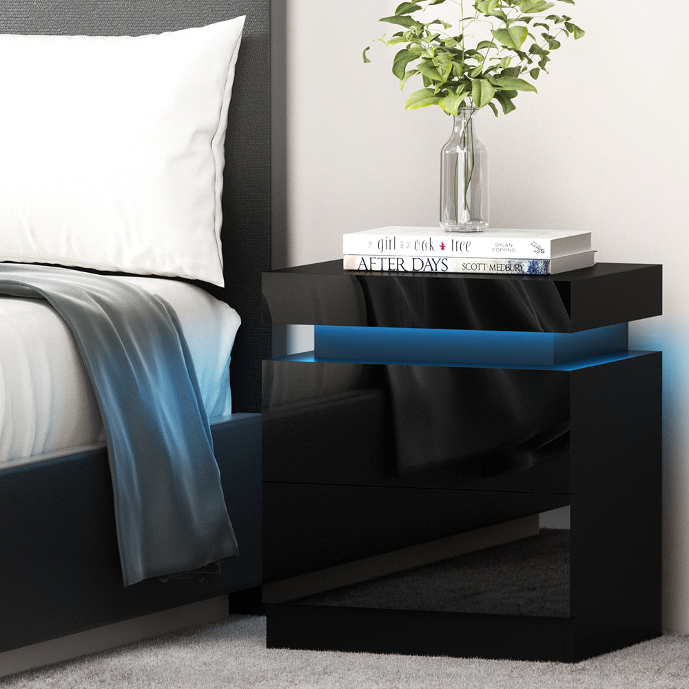 Black nightstand with blue accent next to a bed with white pillows and gray blanket.