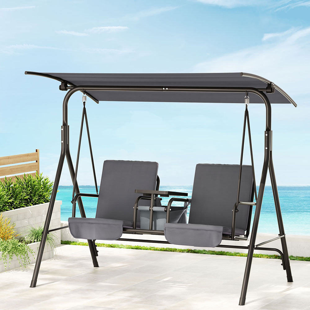 Deriate 2-Seater Outdoor Swing Chair | Grey on a patio with a beach view.