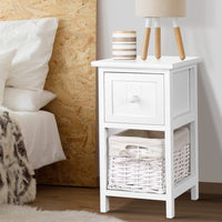 White nightstand with a drawer and wicker basket next to a bed with wooden headboard.