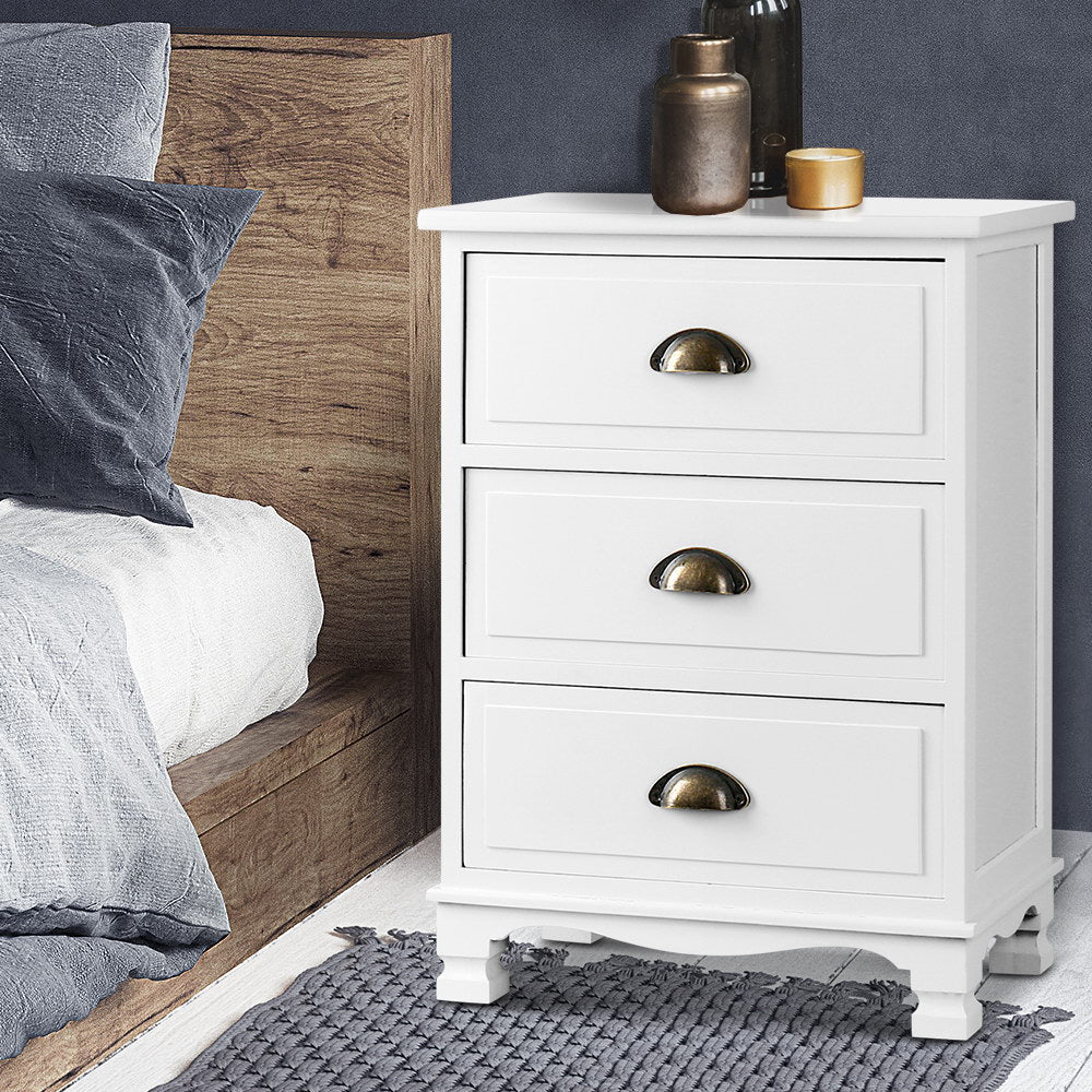 White nightstand with gold handles next to a bed with gray bedding.
