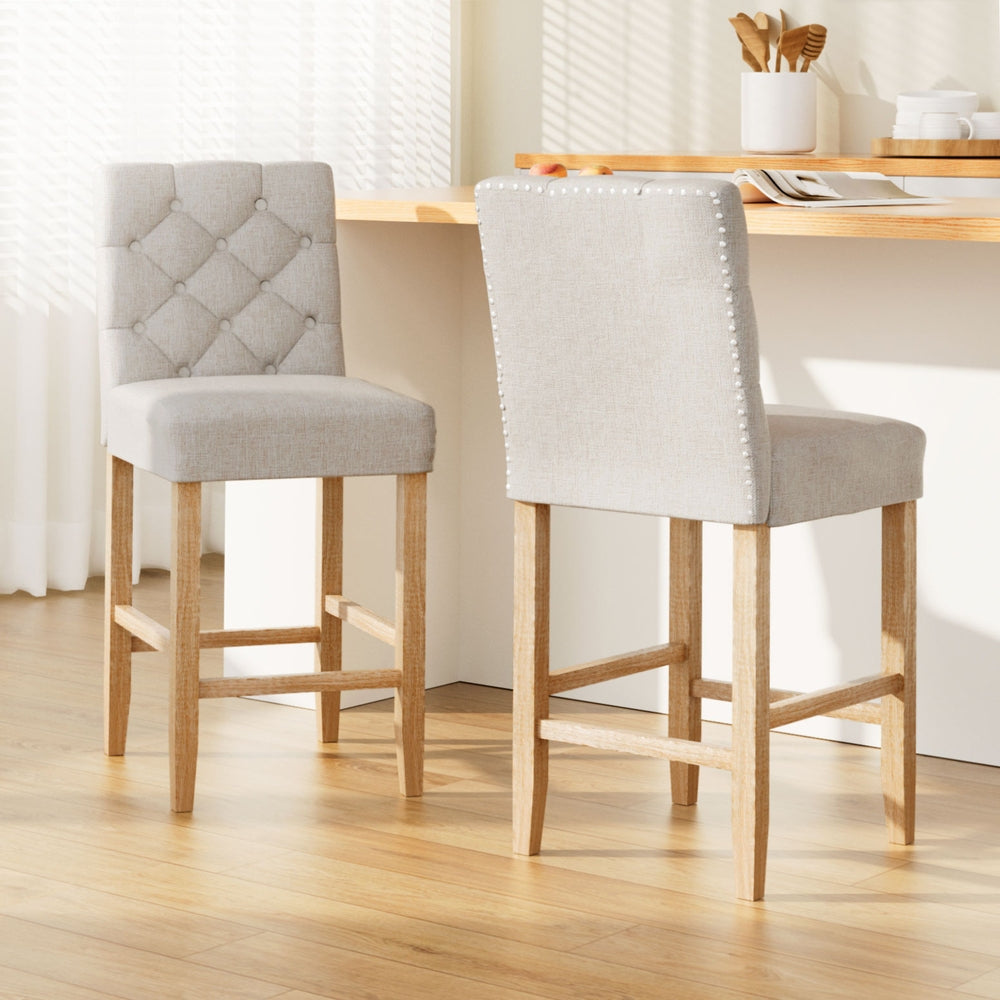 Two gray cushioned bar stools with wooden legs in front of a wooden dining table.