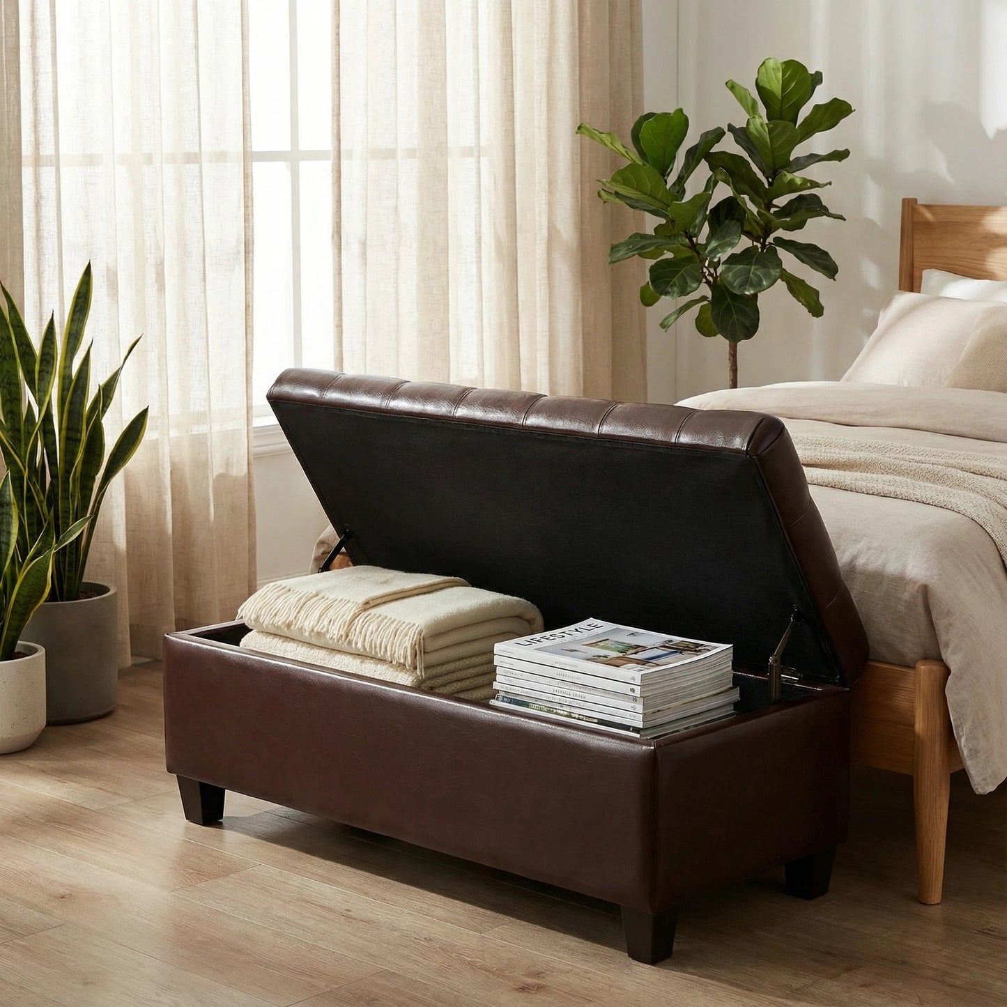 Brown leather storage bench in a bedroom with folded blankets and magazines, surrounded by plants.