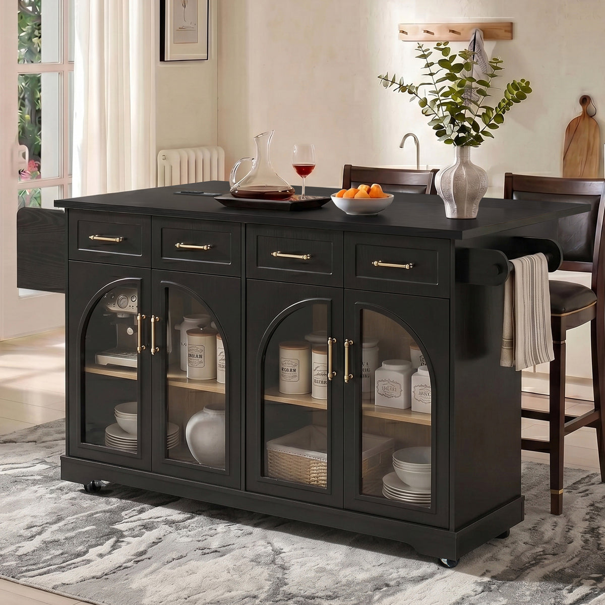 Black kitchen island with four arched glass doors and gold-tone handles, styled beside stools in a softly lit room.