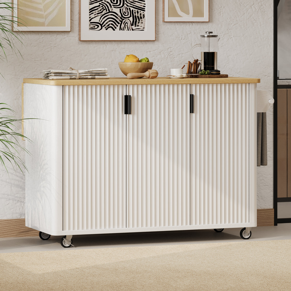 White fluted kitchen island with a pale wood-look countertop, black handles, and casters beneath framed wall art.